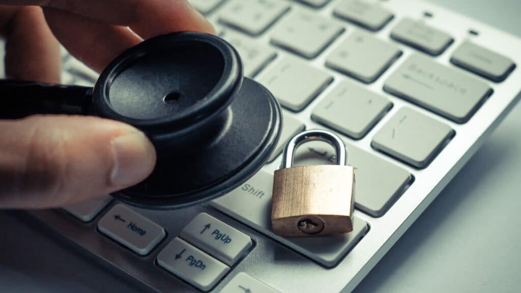 hand holding a stethoscope over computer keyboard with a security lock, healthcare data breach concept.