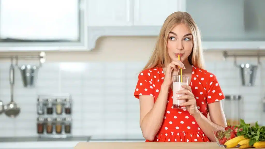 Young woman with glass of delicious milk shake in kitchen