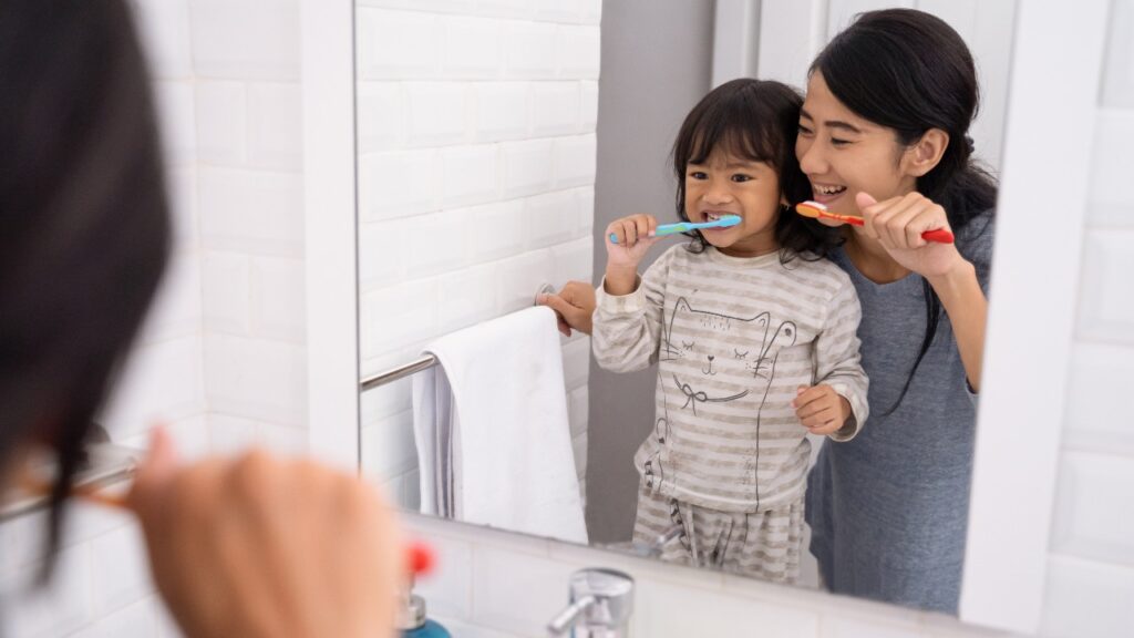 Mother helping toddler brush teeth
