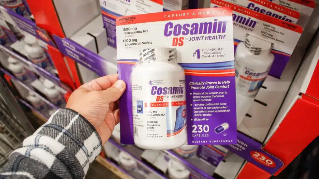 A view of a hand holding a package of Cosamin DS capsules, on display at a local big box grocery store.
