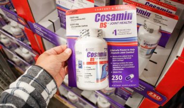 A view of a hand holding a package of Cosamin DS capsules, on display at a local big box grocery store.