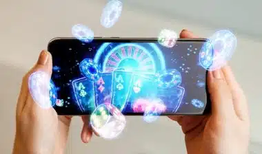 online casino, in a man's hand a smartphone with playing cards, roulette and chips, black-neon background.