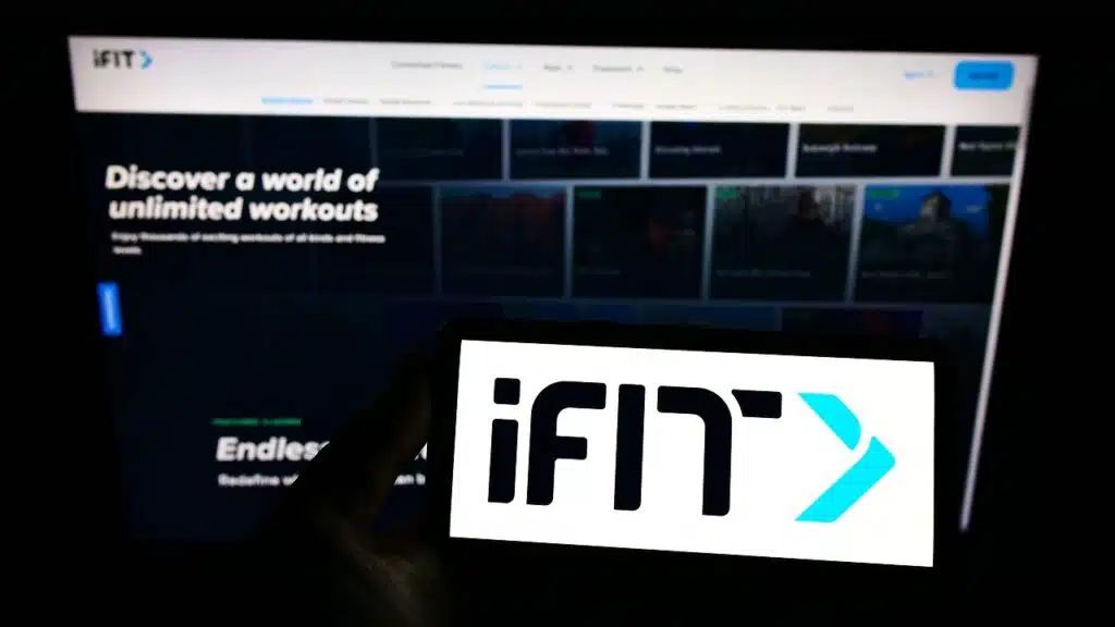 Person holding smartphone with logo of US fitness company iFIT Inc. on screen in front of website.