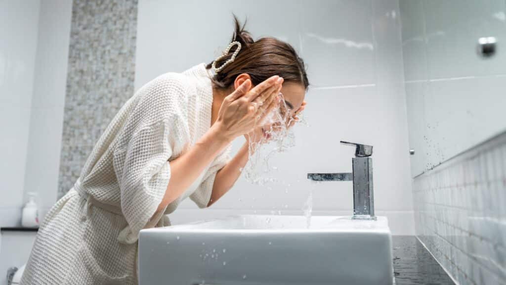 woman washing her clean face with facial foam and water.