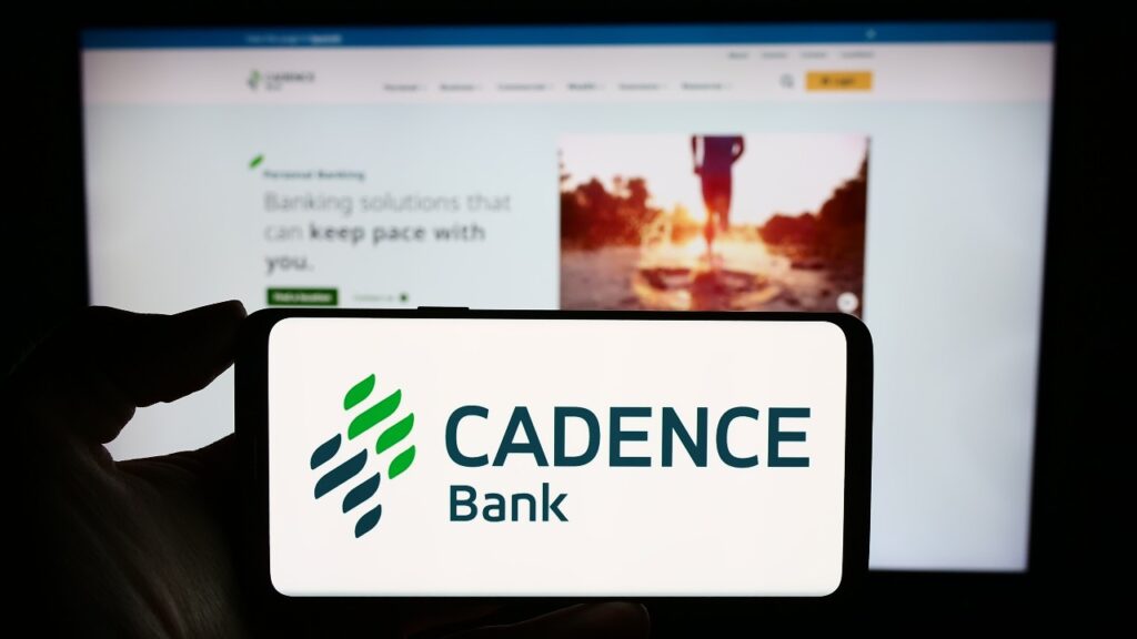 Person holding smartphone with logo of US financial services company Cadence Bank in front of website.