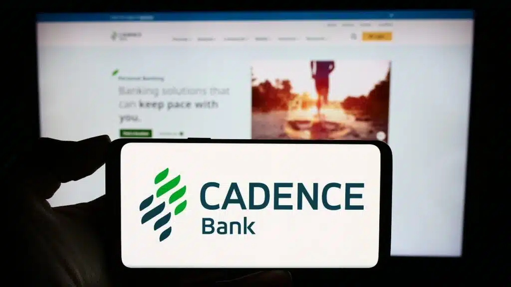 Person holding smartphone with logo of US financial services company Cadence Bank in front of website.