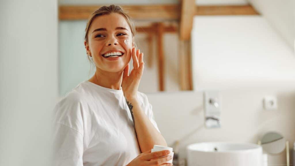young woman taking care of skin by applying moisturizer cream