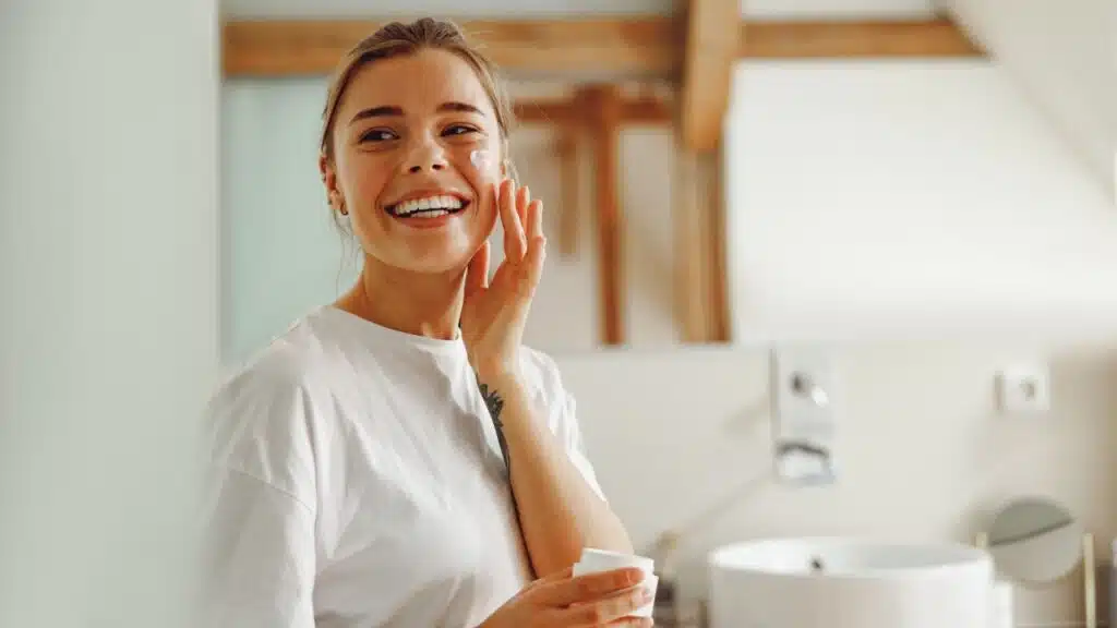 young woman taking care of skin by applying moisturizer cream