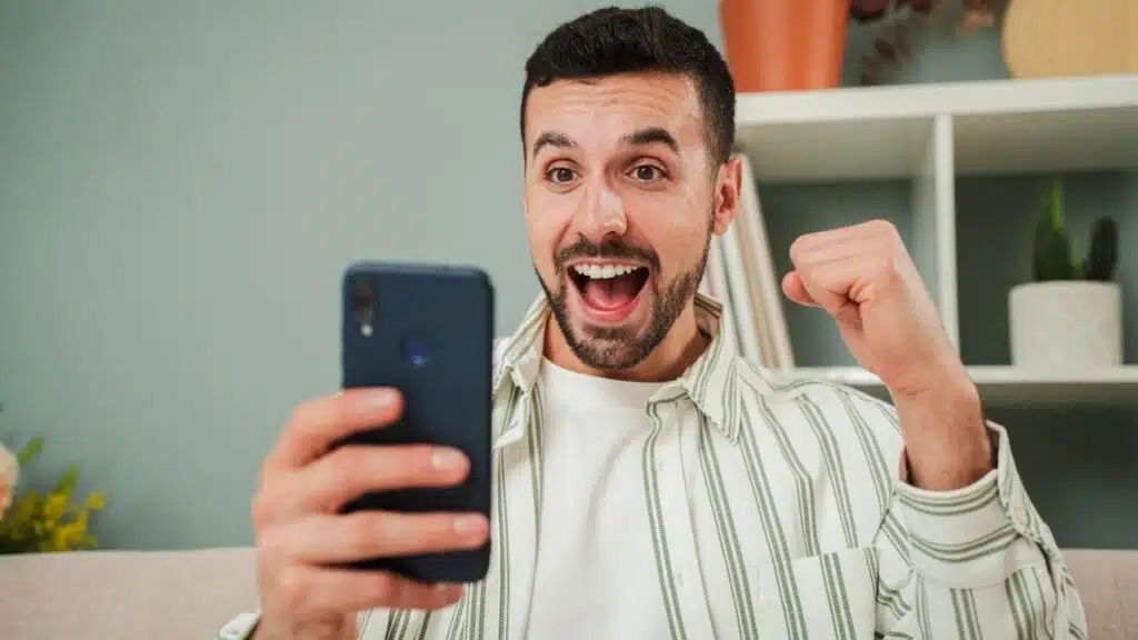 man celebrating that he has won a sports bet while checking the result on a smartphone app.