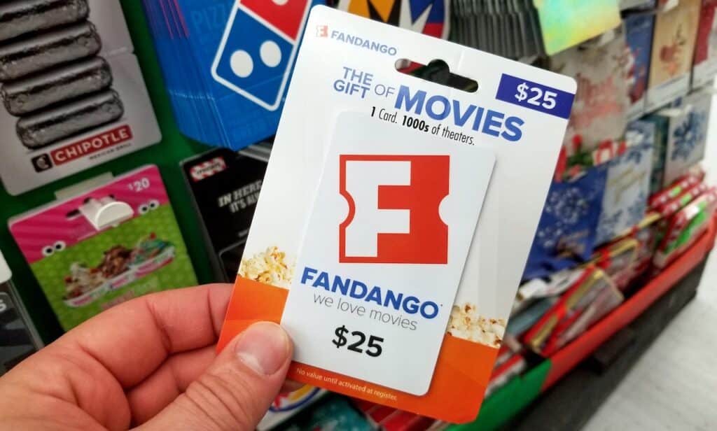 fandango gift card in a hand over a shelves with different giftcards in a Walmart store.