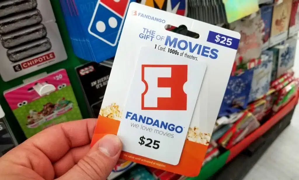 fandango gift card in a hand over a shelves with different giftcards in a Walmart store.