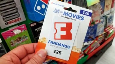 fandango gift card in a hand over a shelves with different giftcards in a Walmart store.