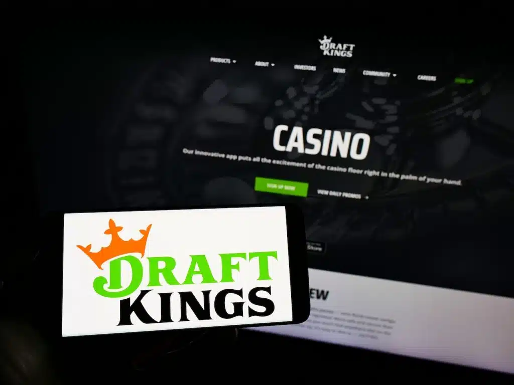 Person holding mobile phone with logo of US sports betting company DraftKings Inc. on screen in front of business web page.