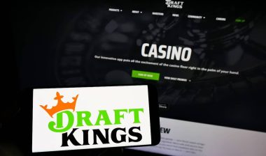 Person holding mobile phone with logo of US sports betting company DraftKings Inc. on screen in front of business web page.