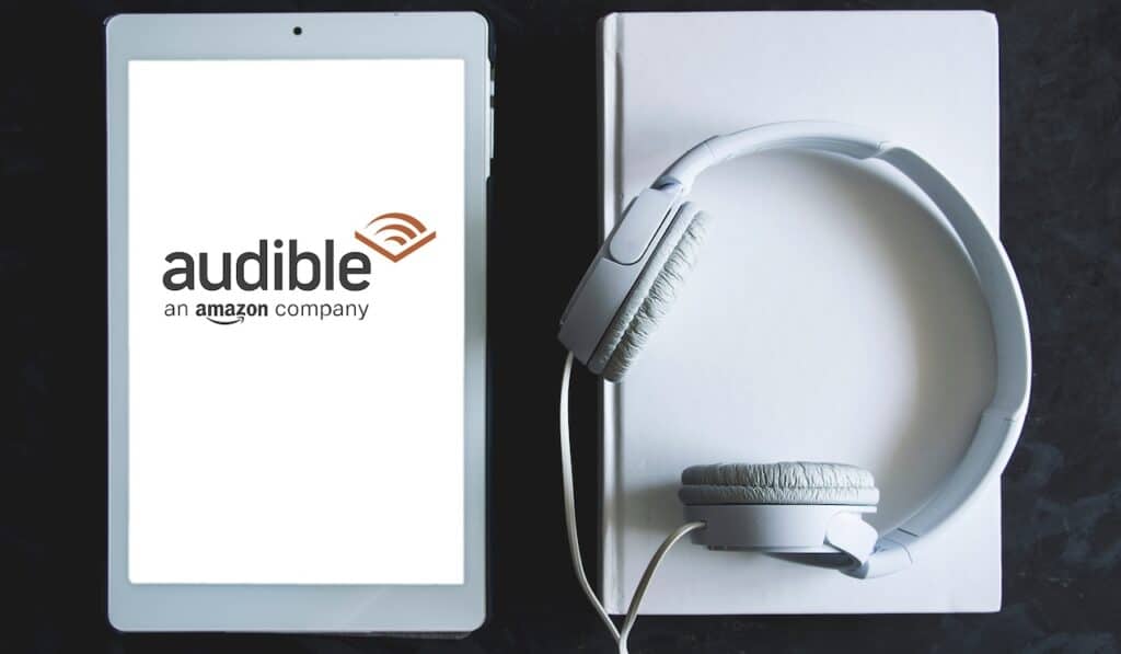Audible app screen logo on a tablet, next a white headphones.