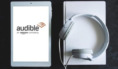 Audible app screen logo on a tablet, next a white headphones.