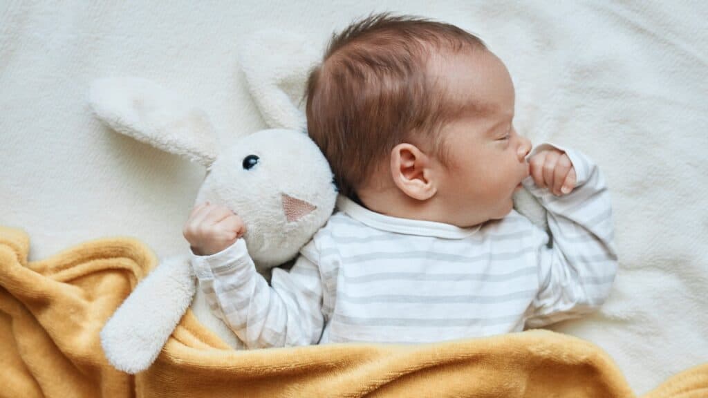 Newborn baby boy in bed sleeping under yellow soft blanket with fluffy rabbit toy
