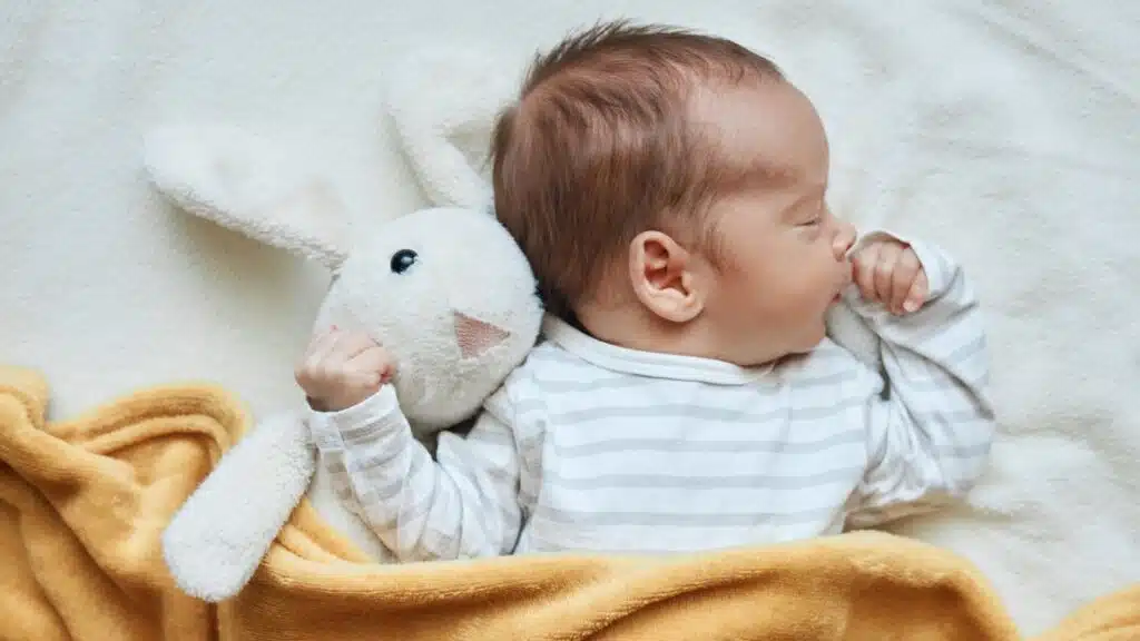 Newborn baby boy in bed sleeping under yellow soft blanket with fluffy rabbit toy