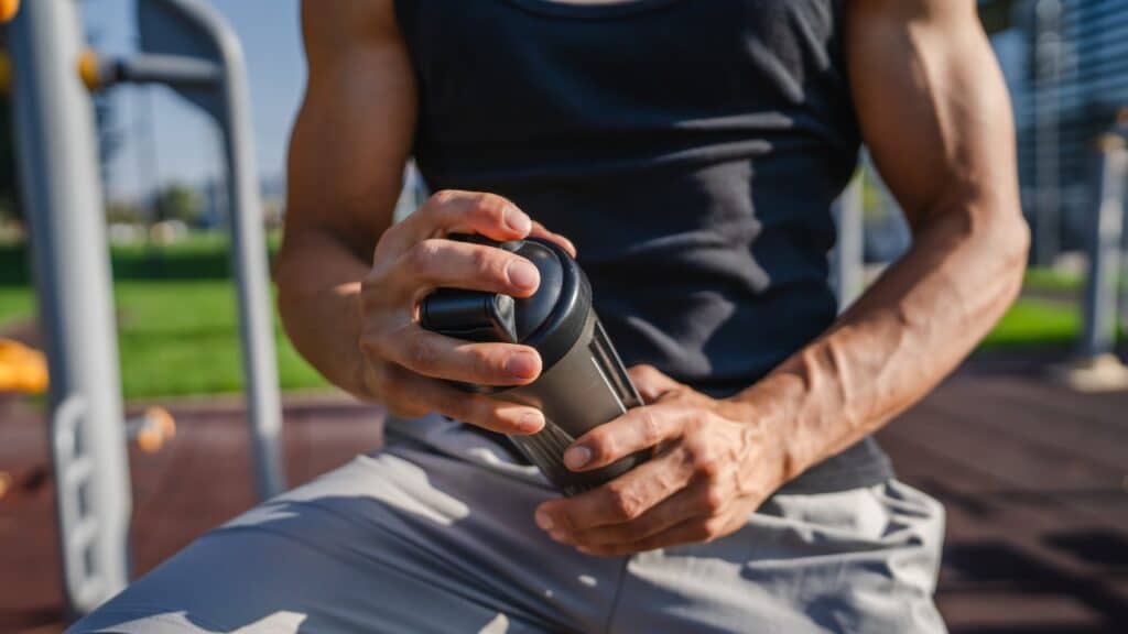 caucasian man young male athlete take a brake during outdoor training in the park outdoor gym hold supplement shaker in hand