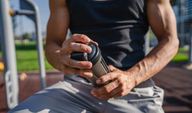 caucasian man young male athlete take a brake during outdoor training in the park outdoor gym hold supplement shaker in hand, representing recent protein class actions.