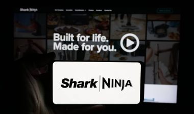 Person holding cellphone with logo of US technology company SharkNinja on screen in front of business webpage.