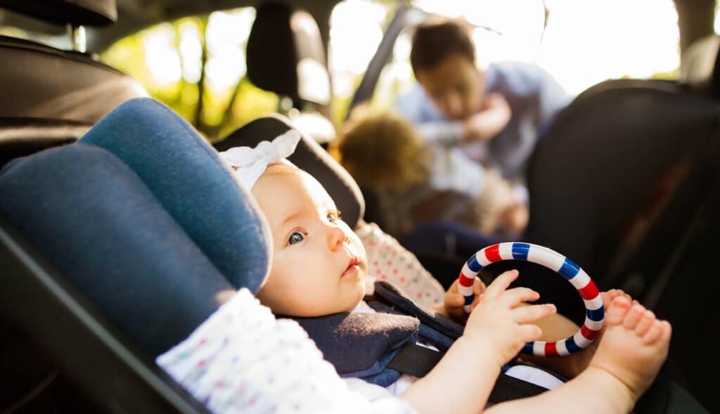 Little baby girl fastened with security belt in safety car seat.