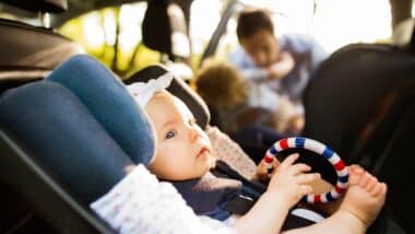 Little baby girl fastened with security belt in safety car seat.