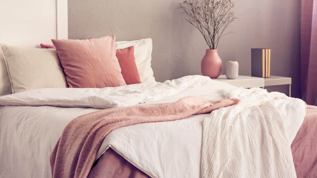 King size bed with pastel pink and white bedding in trendy bedroom
