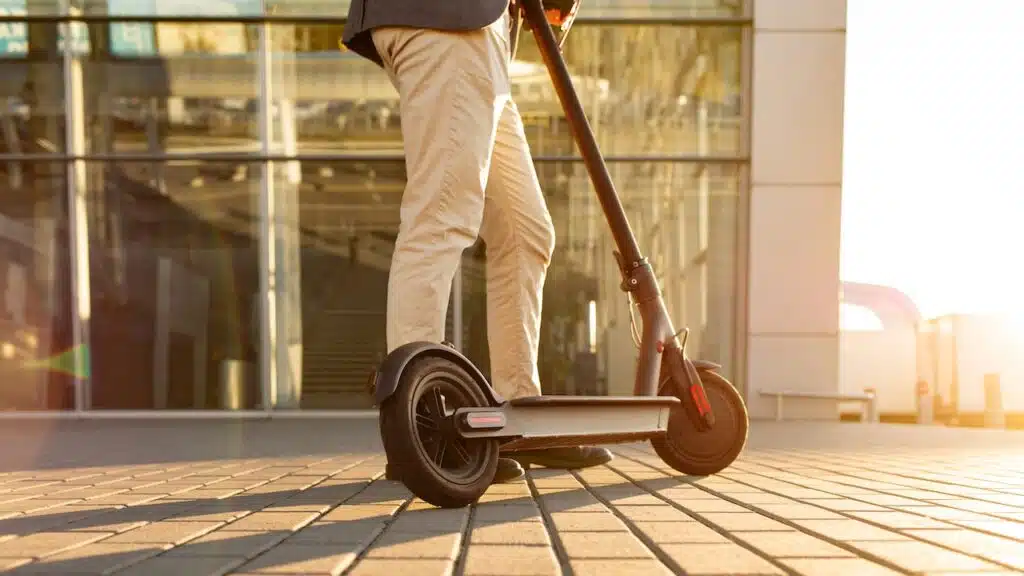 Legs of a man standing on e-scooter parked on sidewalk at cityscape on the sunset.