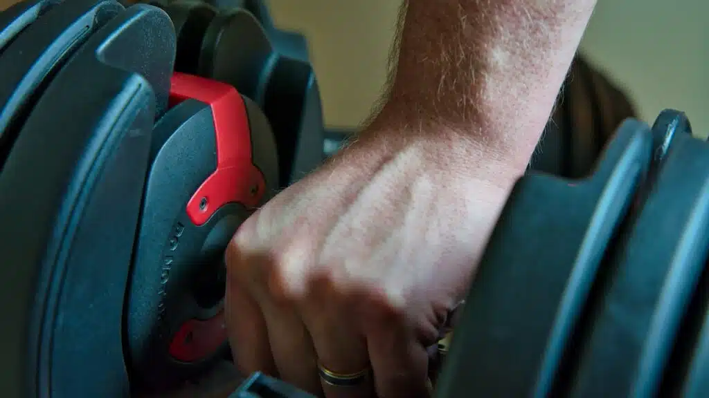 Hand gripping adjustable dumbbells for working out at home.