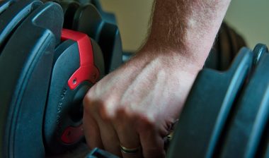 Hand gripping adjustable dumbbells for working out at home.