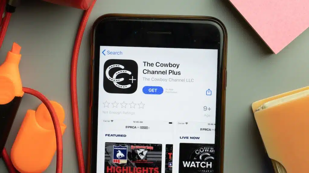 Phone screen close-up with The Cowboy Channel Plus mobile app logo on display.