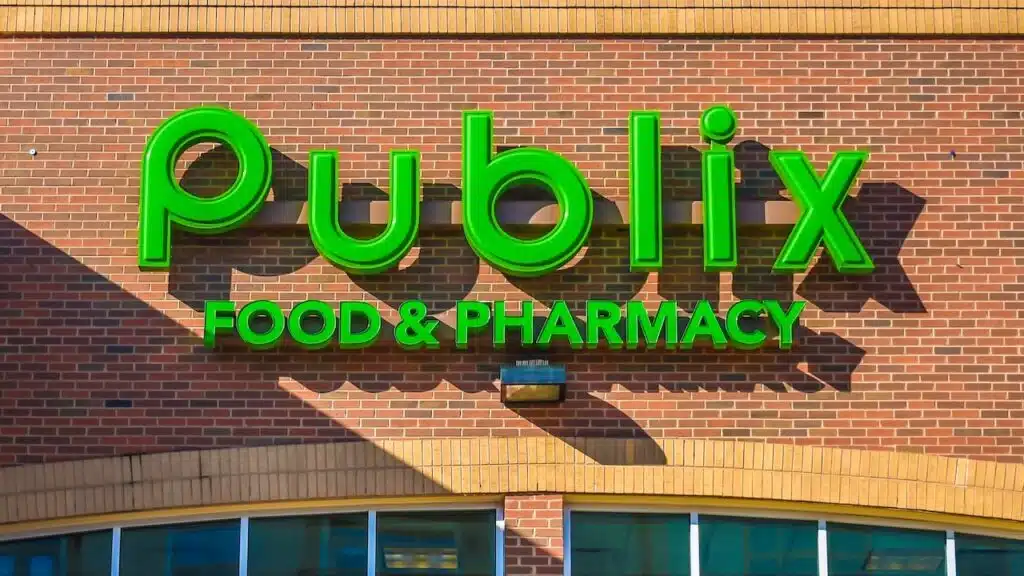 Horizontal, medium closeup of "Publix" Food and Pharmacy store's exterior facade brand and logo signage above arched windows in the soft light of the setting sun.