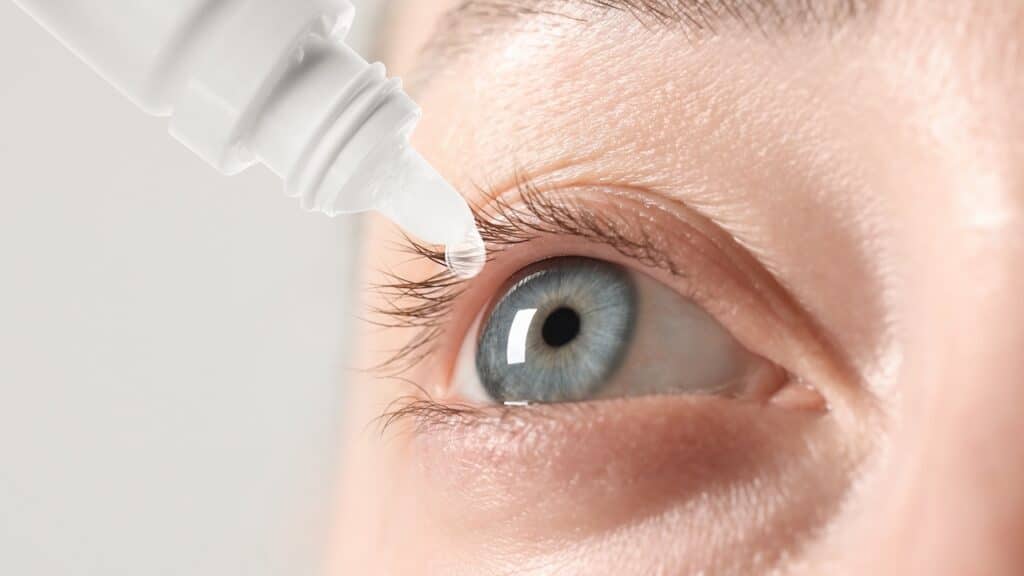 Woman applying eye drops on light background, closeup
