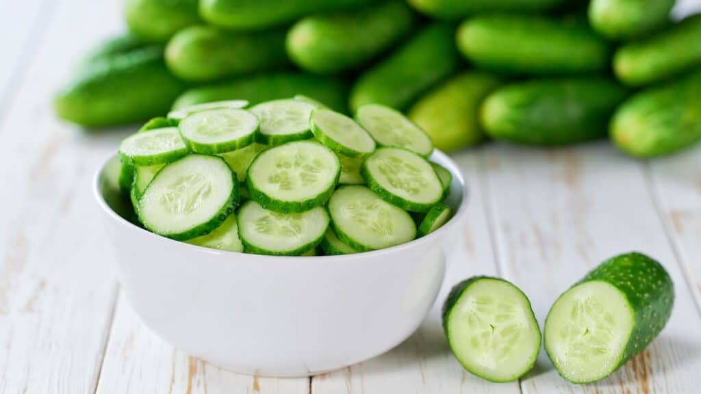 Organic cucumbers slices in a ceramic bowl on a light table, selective focus.