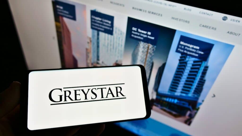 Person holding cellphone with logo of US apartment company Greystar Real Estate Partners on screen in front of webpage.