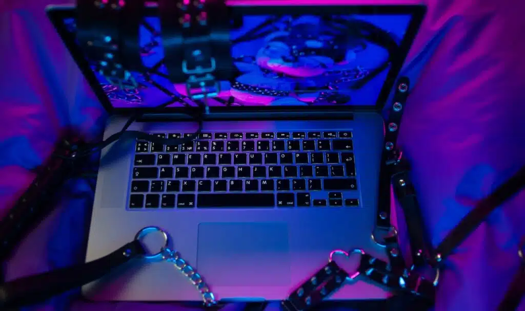A set of BDSM toys for sex on a laptop on a bright neon background.