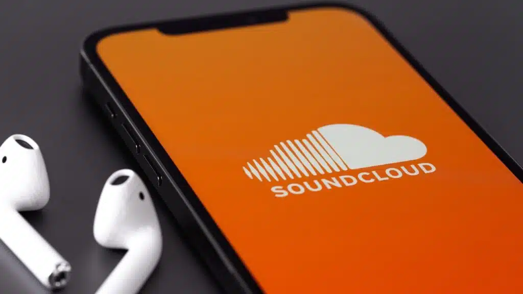 Soundcloud logo mobile app on screen smartphone iPhone and AirPods headphones macro closeup.