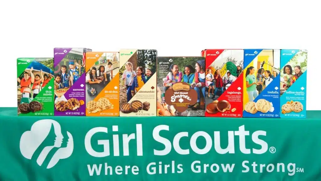 Boxes of Little Brownie Baker Girl Scout cookies on table in mock both sale with GS logo on green table cloth. Isolated.