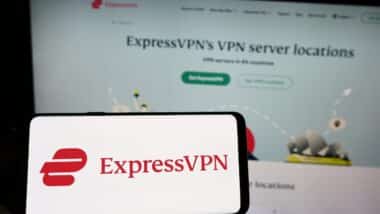 Person holding cellphone with logo of VPN service company ExpressVPN on screen in front of business webpage.