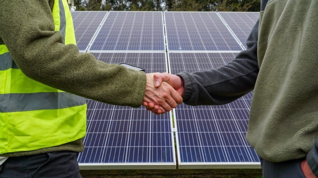 Two people shaking hands in front of solar panels. Renewable energy agreement.