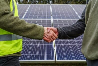 Two people shaking hands in front of solar panels. Renewable energy agreement.