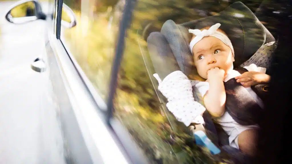Little baby fastened with security belt in safety car seat.