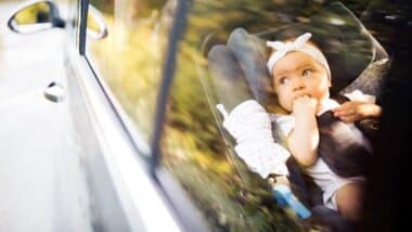 Little baby fastened with security belt in safety car seat.
