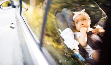 Little baby fastened with security belt in safety car seat.