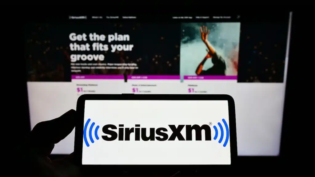 Person holding smartphone with logo of US broadcasting company Sirius XM Holdings Inc. on screen in front of website.