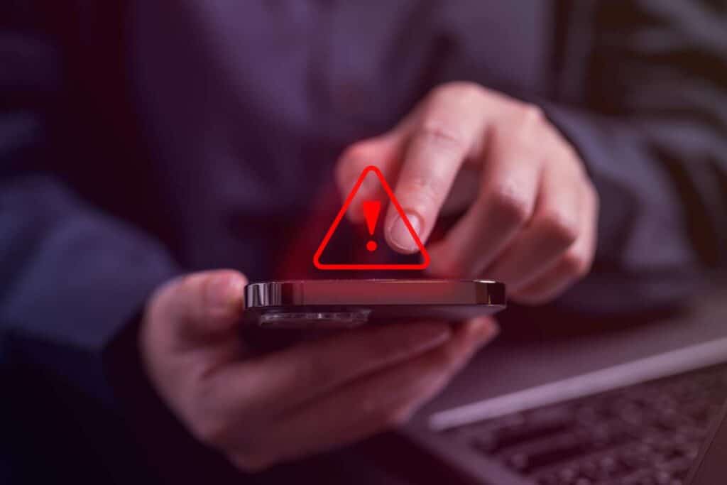 Close up of hands using a smartphone with a warning symbol overlay, representing the MarinHealth Medical Center settlement.
