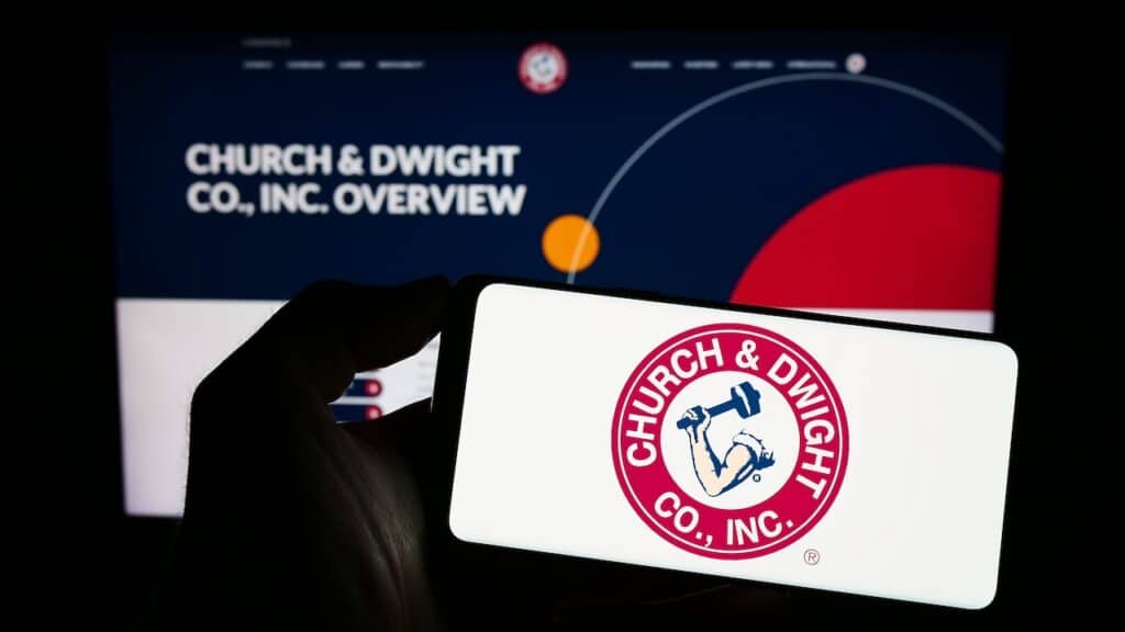 Person holding smartphone with logo of US consumer goods company Church Dwight Co. Inc. on screen in front of website. Focus on phone display.