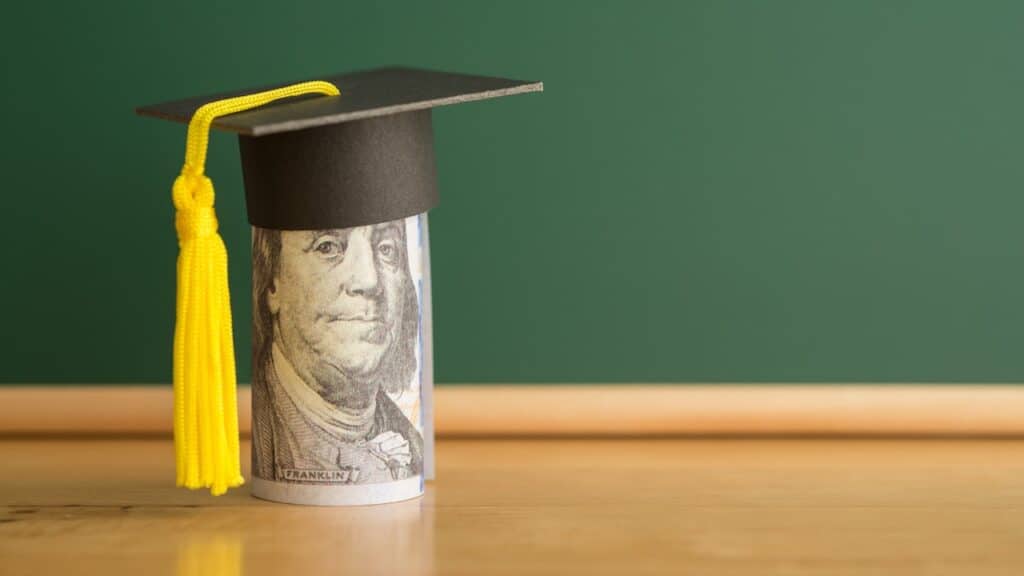 US dollars banknote wears graduation cap chalkboard background in classroom