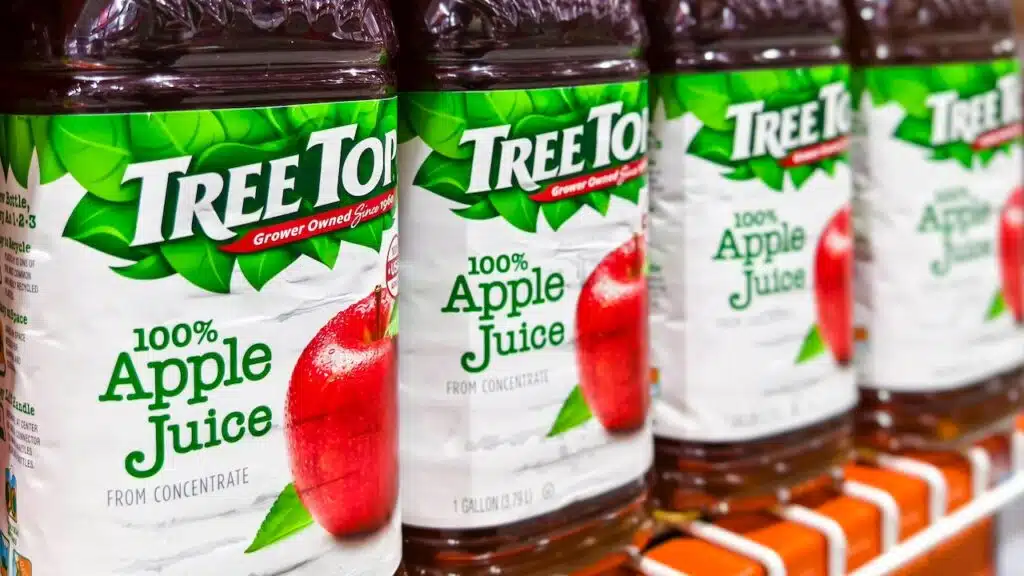 Tree Top Apple juice bottles lined up on a store shelf, ready for purchase.